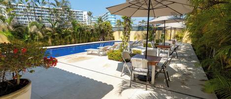 Un área junto a la piscina con sillones de descanso, sombrillas y una planta en maceta.