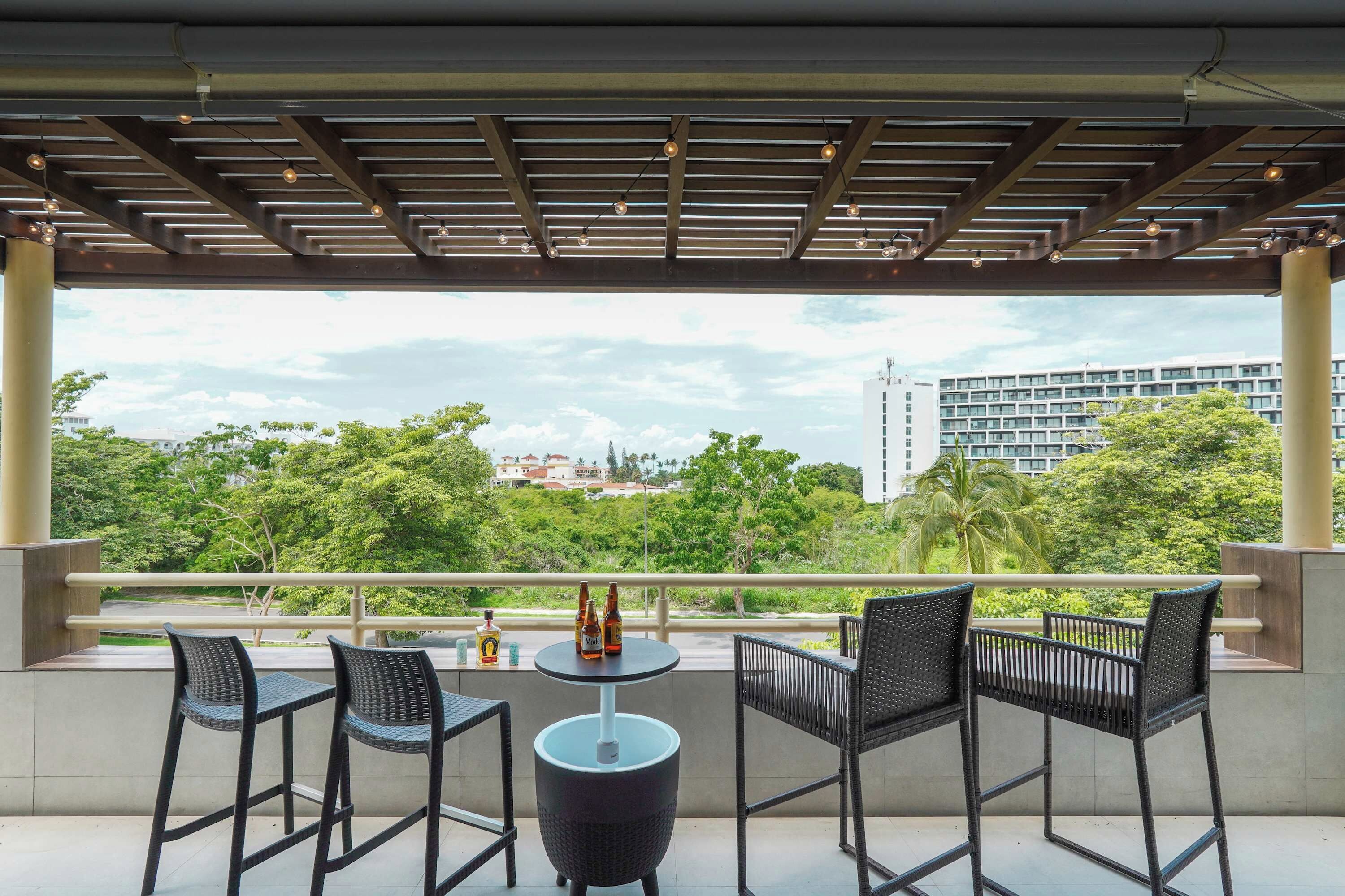 A balcony with four chairs and a table, overlooking a cityscape with greenery and buildings.
