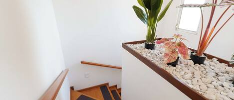 Una escalera con escalones de madera y una pared blanca. Hay plantas en macetas en la barandilla y una ventana con vistas.