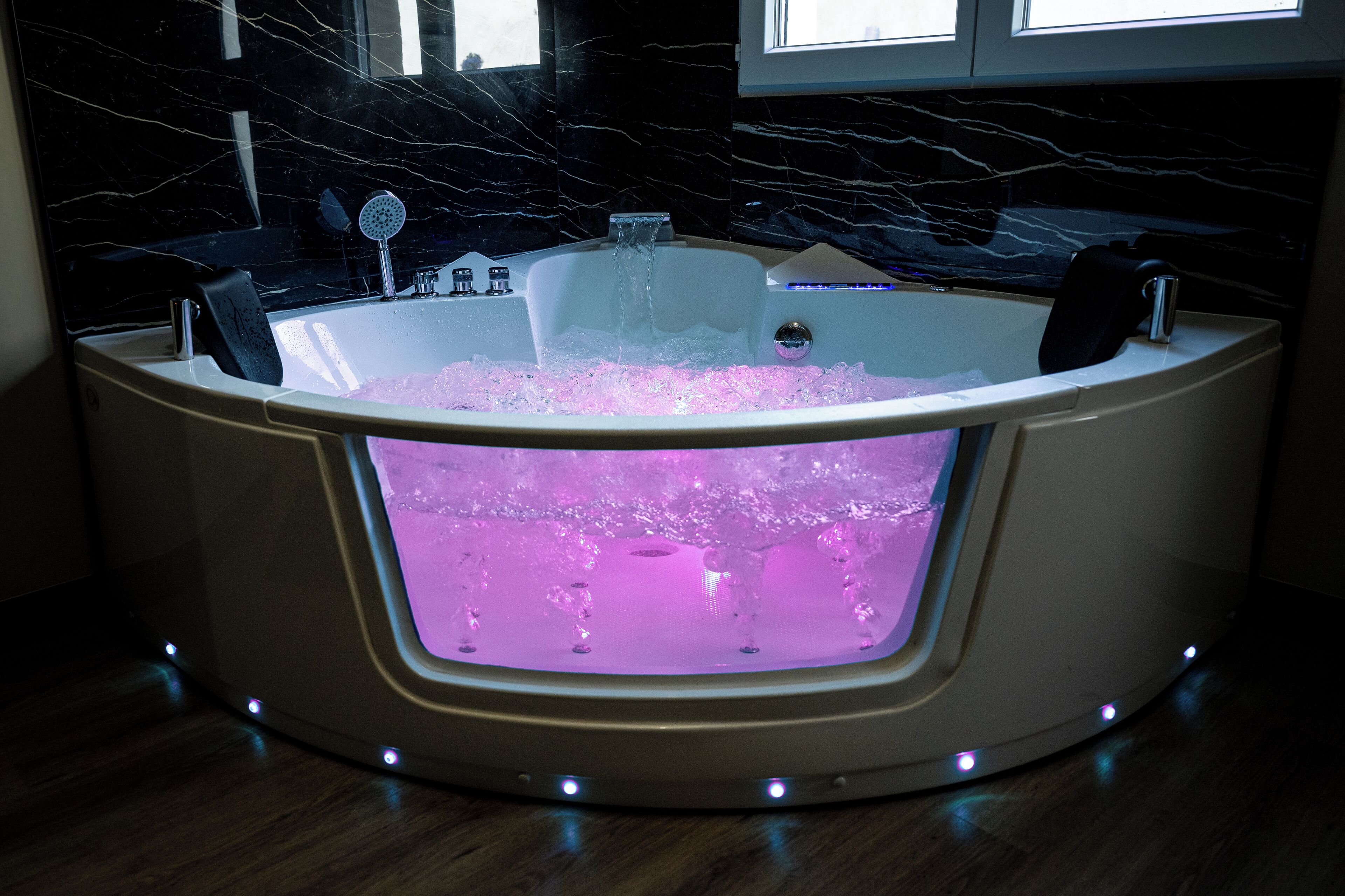 A modern bathroom with a marble wall, a bathtub filled with water, and a built-in massage chair.