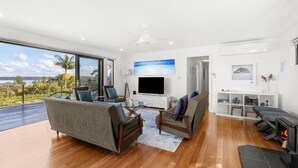 A modern living room with a large TV, comfortable seating, a fireplace, and a balcony with a scenic view. - Lakeviews - Pet Friendly with Fireplace (Culburra Beach)