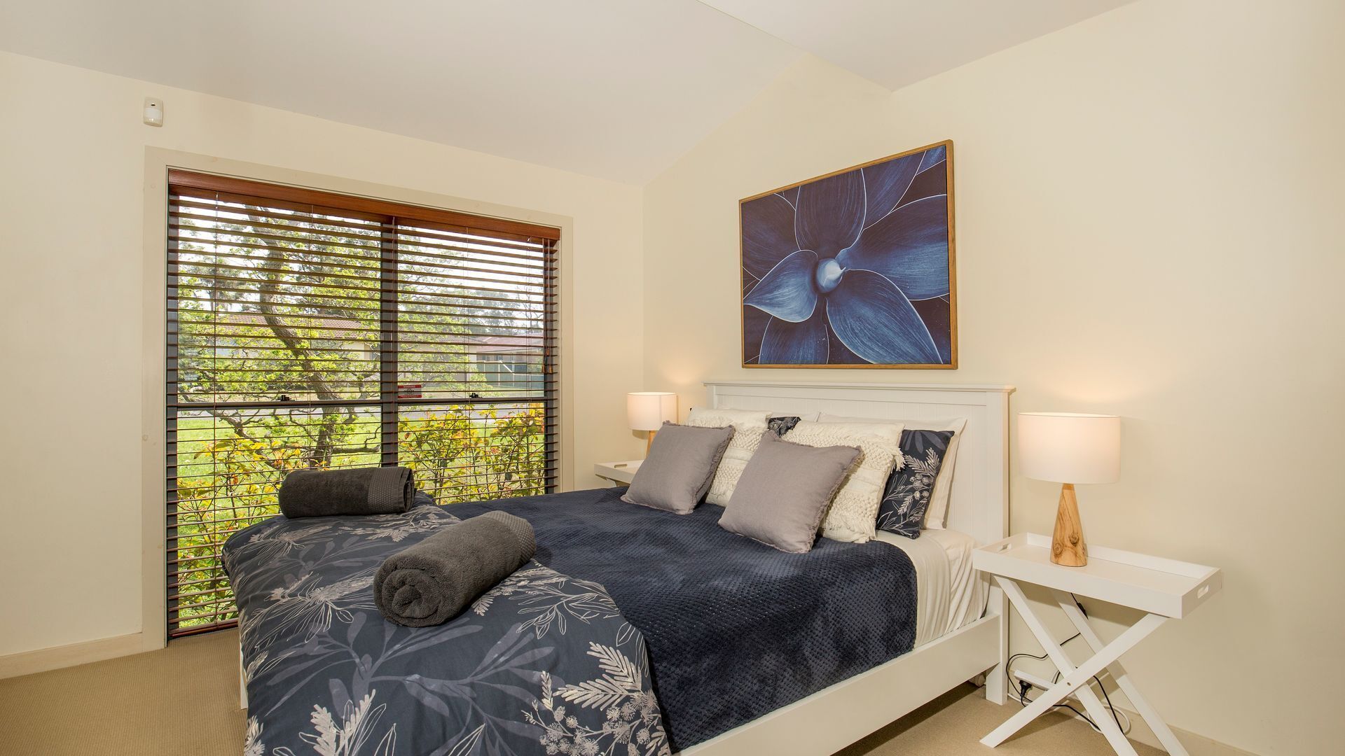 A bedroom with a bed, a bedside table, a lamp, and a window with blinds.