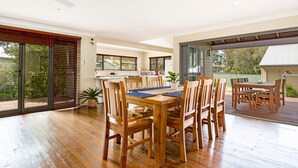 Un vaste espace de salle à manger avec une table et des chaises en bois, de grandes portes-fenêtres coulissantes donnant sur une terrasse, et une vue sur la verdure environnante.