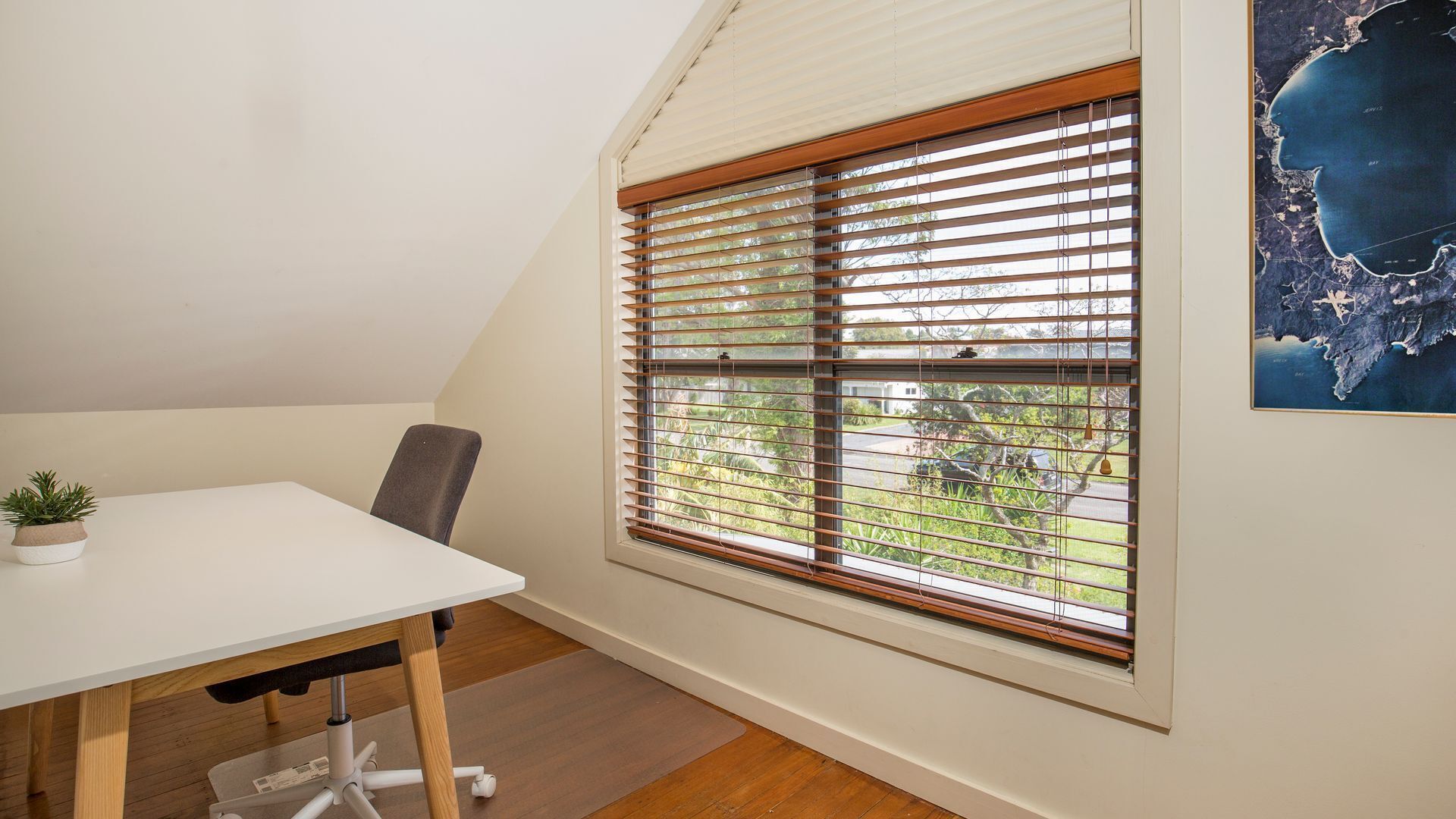 A room with a white desk, a chair, a potted plant, and a window with blinds.