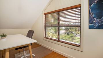A room with a white desk, a chair, a potted plant, and a window with blinds.