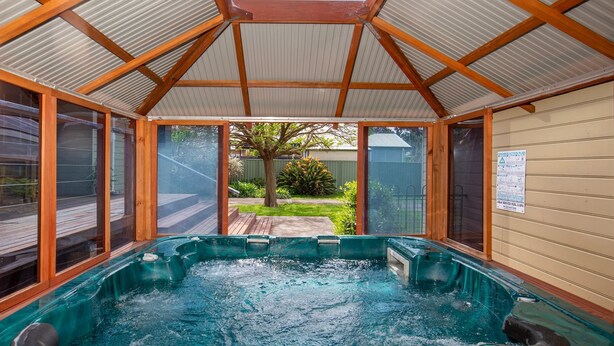 Un bain à remous doté d’un toit en bois et de parois en verre, entouré d’une terrasse.
