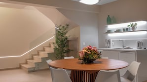 Eine moderne Küche mit weißen Geräten, ein Essbereich mit einem Holztisch und weißen Stühlen sowie eine Treppe mit Glastrennwand.