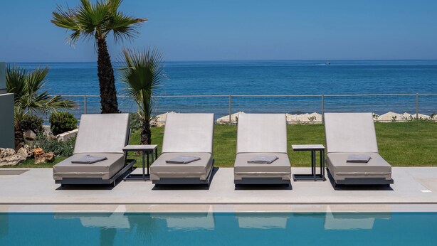 Ein Poolbereich mit vier Liegestühlen und einer Palme mit Blick auf das Meer.