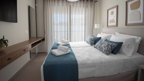 Ein modernes Hotelzimmer mit einem großen Bett, einem Flachbildfernseher, einem Nachttisch und einem Fenster mit transparenten Vorhängen.