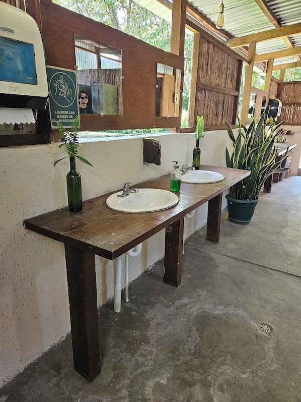 A restroom with two sinks, a mirror, and a soap dispenser. - Tres Volcanes (Santa Ana)