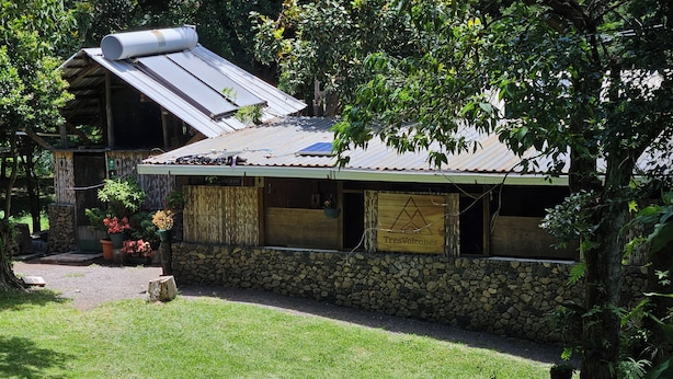 A rustic building with a sloped metal roof, stone walls, and a wooden signboard.