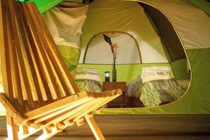 Una tienda de campaña con una cama en su interior, una mesita con una lámpara y una silla de madera.