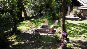 A garden with a fire pit, four wooden chairs, and a table.