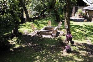 A garden with a fire pit, four wooden chairs, and a table.
