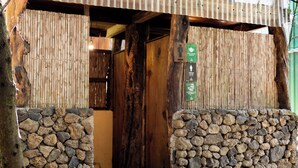 A rustic wooden entrance with a stone wall on one side and a bamboo screen on the other.