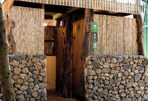 A rustic wooden entrance with a stone wall on one side and a bamboo screen on the other.