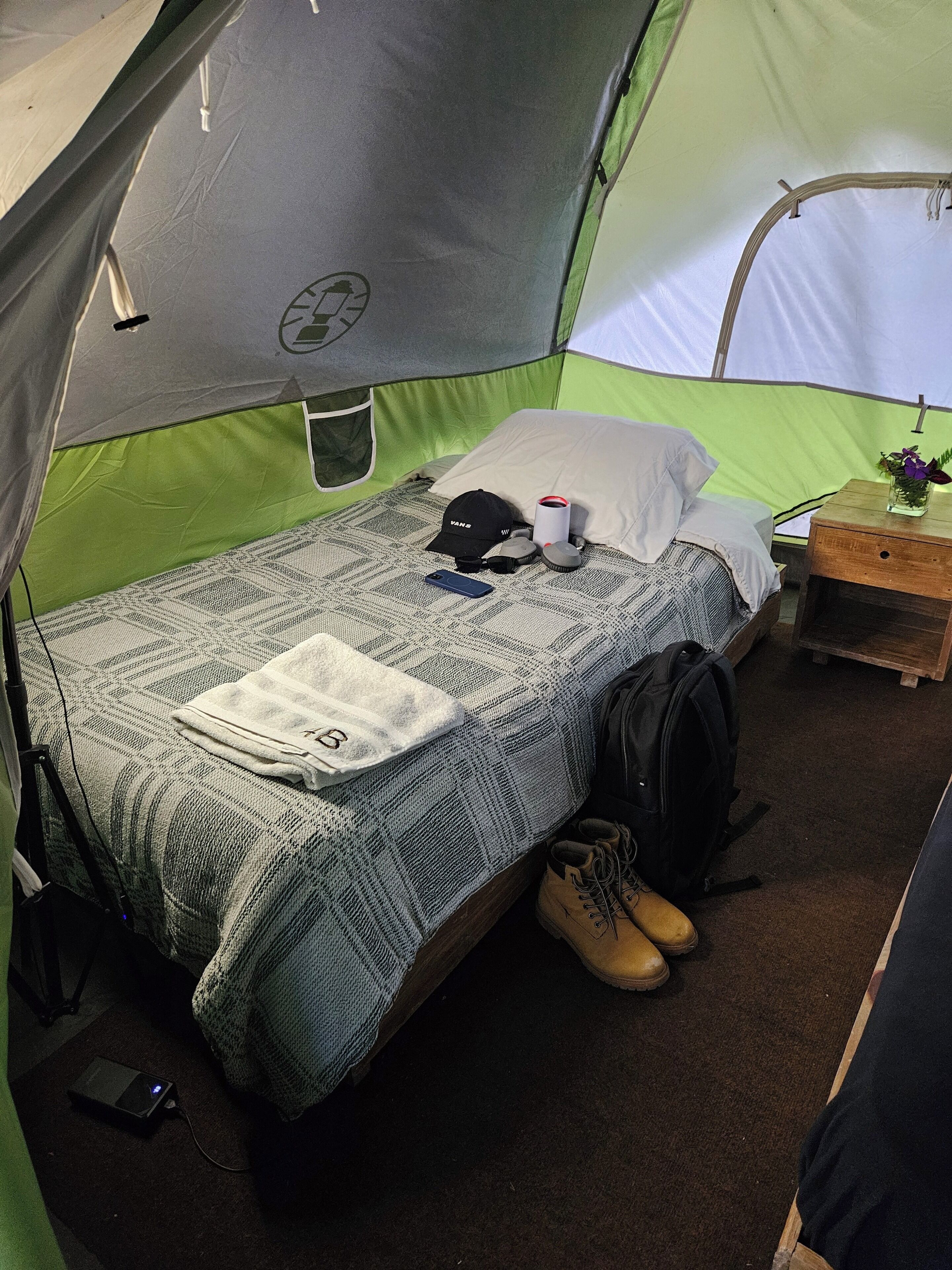 Uma tenda com uma cama, um travesseiro, uma xícara, um boné, uma mochila e um par de botas.