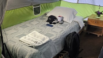 Uma tenda com uma cama, um travesseiro, uma xícara, um boné, uma mochila e um par de botas.