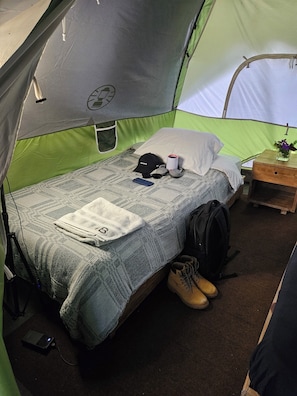 A tent with a bed, a pillow, a cup, a cap, a backpack, and a pair of boots. - Tres Volcanes (Santa Ana)