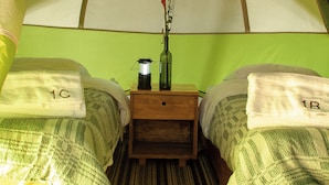 A tent with two beds, each with a pillow labeled '1C' and '1B'. A small table with a candle and a vase with flowers is in the center.