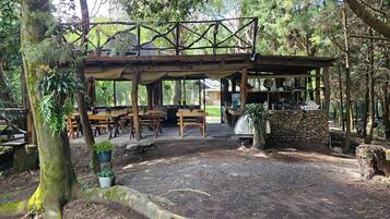 An outdoor wooden structure with tables and benches, surrounded by trees.