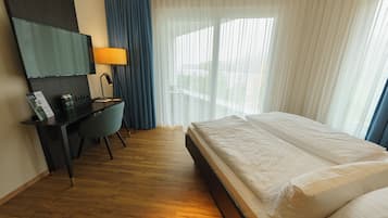 A hotel room with a bed, a desk with a chair, a TV, and a window with curtains.