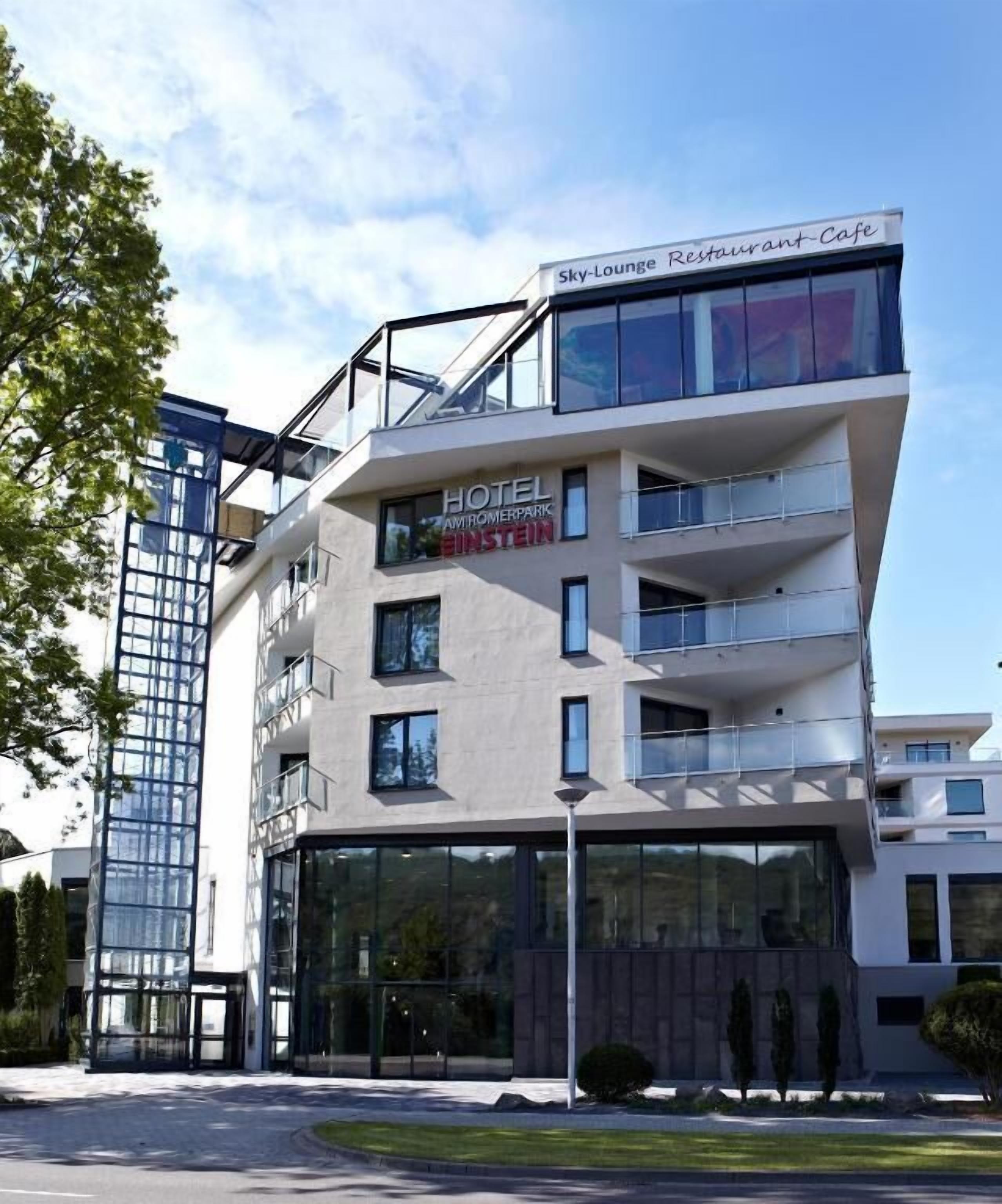Un hôtel moderne à la façade en verre, nommé « Hôtel Amoreparco Einstein », qui comprend un restaurant-café situé au dernier étage.