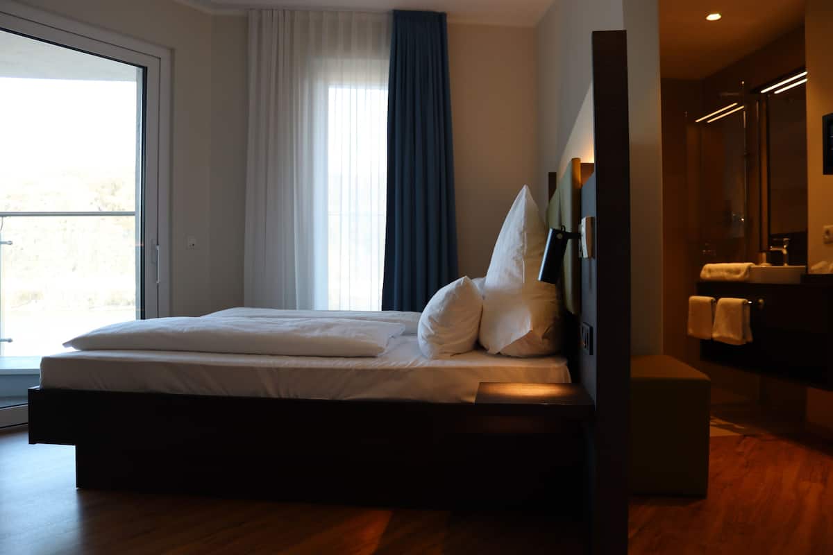 Ein modernes Hotelzimmer mit einem großen Bett, einem Badezimmer mit Spiegel und Blick ins Freie.