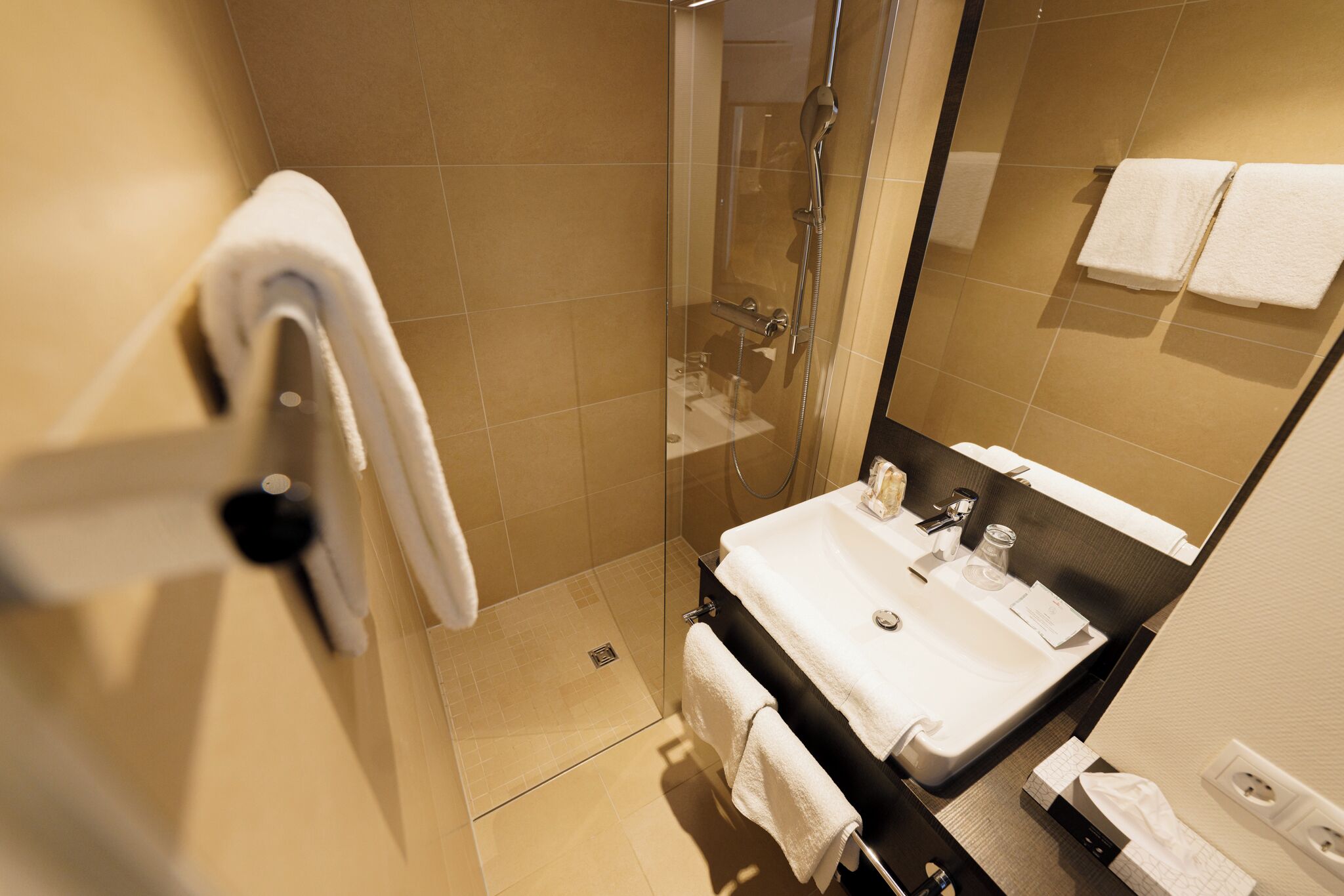 Un bagno moderno con cabina doccia in vetro, un lavabo con specchio e due asciugamani appesi al muro.
