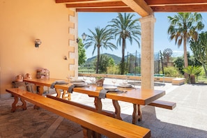 An outdoor patio with wooden tables and benches, a view of palm trees, and a windmill in the background. - Exclusive Villa Es Molinet (5 minutes from the beach) Luxury Villa with pool (Alcúdia)
