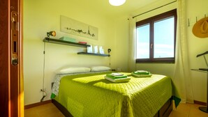 A bedroom with a bed, a window, a shelf with books, and a wall with a picture. - Terrazza Catabbio – Relax & Saturnia Thermal Baths – Garden and Pool (Catabbio)