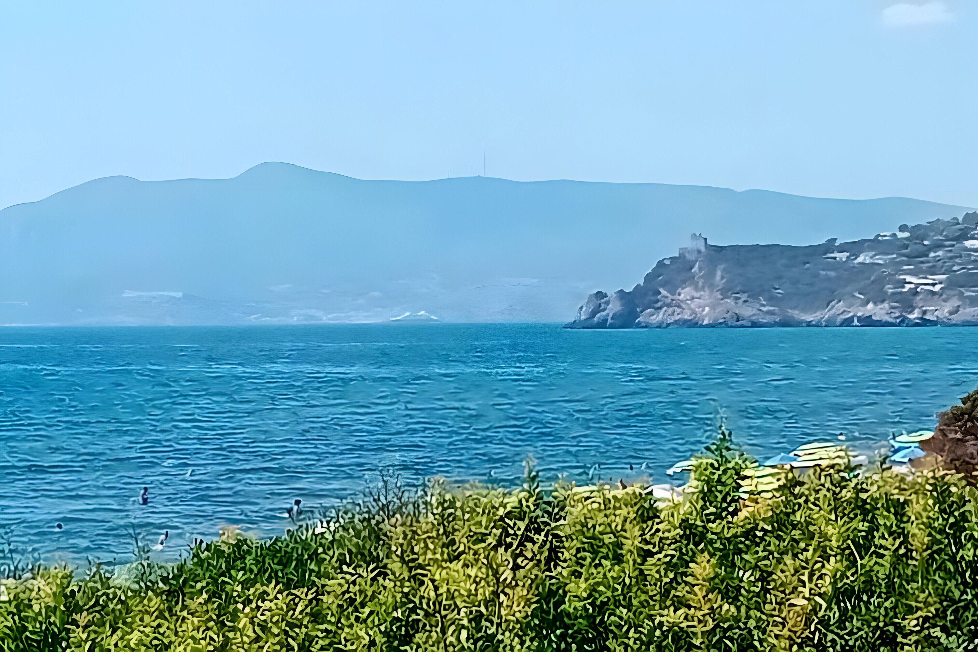 Une vue sur la côte, avec un ciel dégagé, une mer calme et des montagnes à l’horizon.