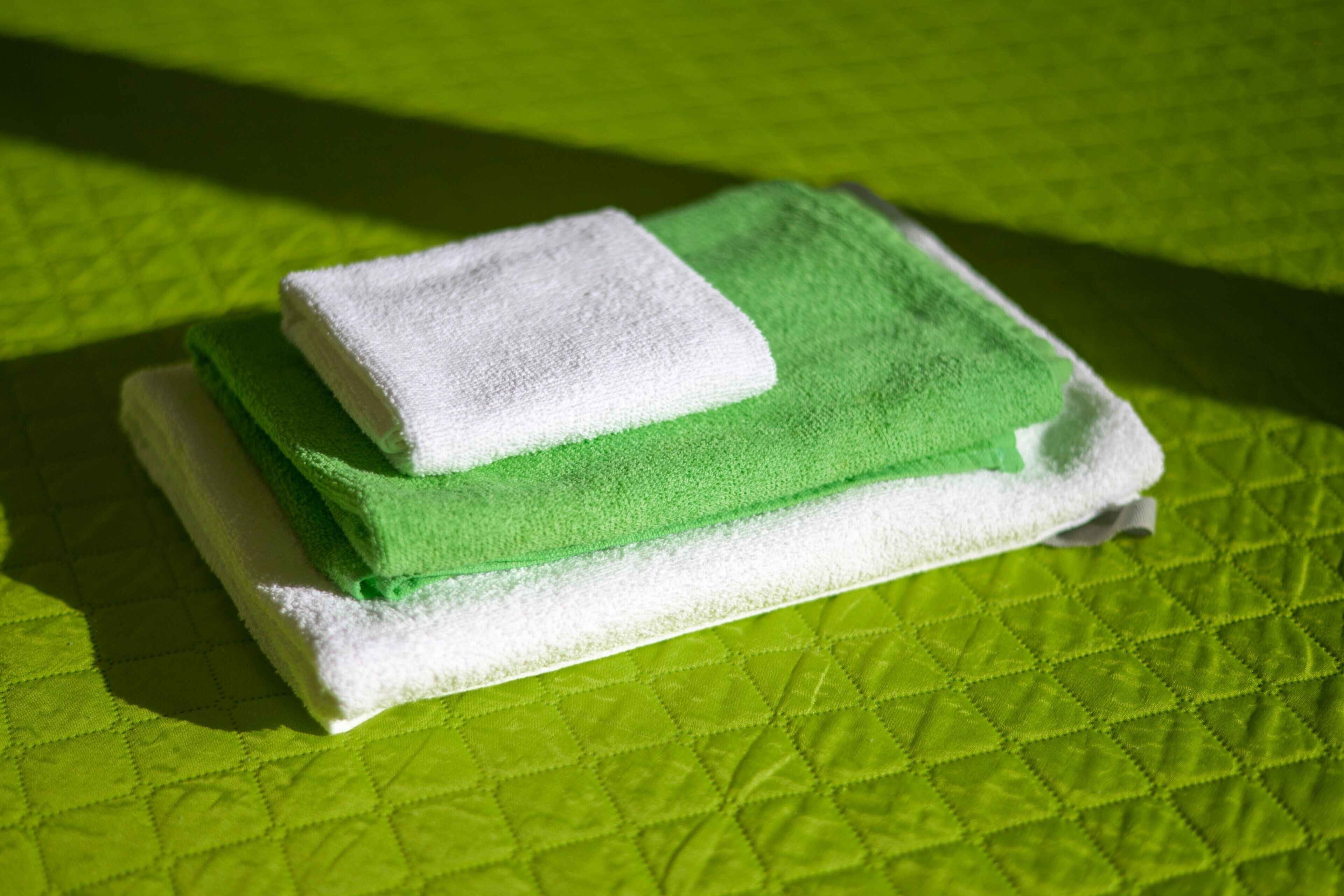 A green quilted bedspread with a neatly folded white towel on top.