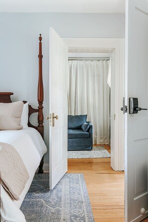 A bedroom with a four-poster bed, a blue sofa, and a white door leading to another room. - Magnolia Suite: Luxury Private Room Downtown (Staunton)