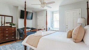 Ein Schlafzimmer mit Himmelbett, einem Schminktisch, einem Fernseher und einem Fenster mit Vorhängen.