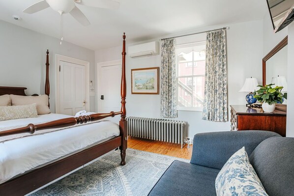 Un dormitorio con cama con dosel, un radiador, un sofá y una ventana con cortinas.