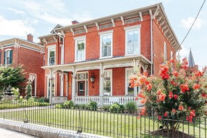 A two-story brick building with a white porch and a number '329' sign. - Magnolia Suite: Luxury Private Room Downtown (Staunton)