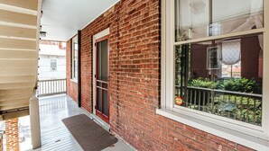 En overdækket veranda med murstensfacade, en rød dør og et vindue med udsigt til grønt.