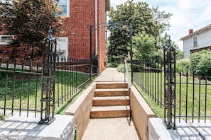 A staircase leading to a brick building with a metal fence and greenery around.