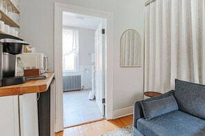 A compact living space with a kitchenette, a sofa, a mirror, and a view into the bathroom. - Magnolia Suite: Luxury Private Room Downtown (Staunton)