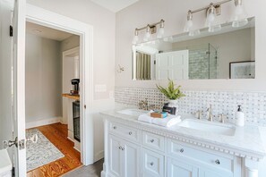 A bathroom with a white vanity, a large mirror, and a shower area. - Magnolia Suite: Luxury Private Room Downtown (Staunton)