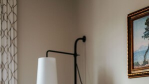 Een keurig opgemaakt bed met een gestreept kussen en een effen kussen, een wandlamp en een ingelijste foto aan de muur.