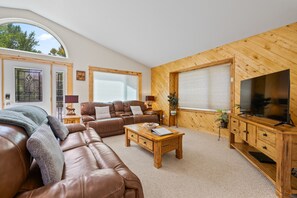 A spacious living room with leather sofas, a wooden coffee table, and a television on a wooden cabinet. - Hot Tub, Game Room, Mtn Views Near Ski & River (South Fork)