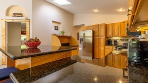 A modern kitchen with granite countertops, wooden cabinets, a stainless steel refrigerator, and a built-in oven.