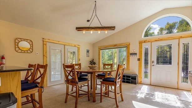 A dining area with a round table and six wooden chairs, a chandelier, and a large arched window.