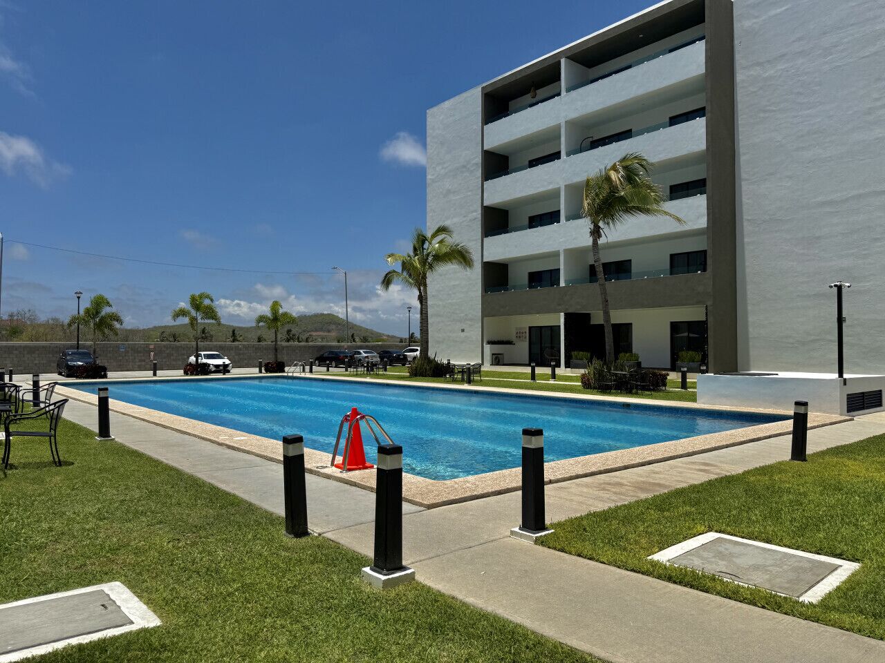 A modern building with a swimming pool, surrounded by a well-maintained lawn and palm trees.
