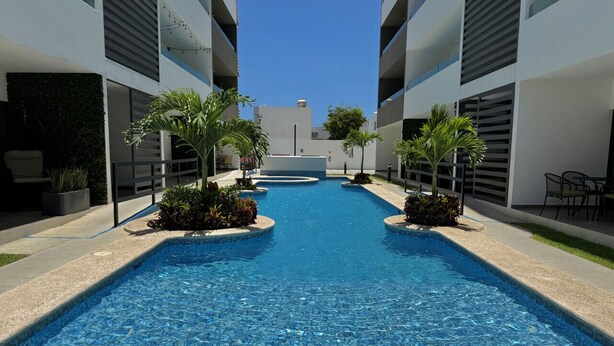 A swimming pool with a clear blue water surface, surrounded by modern buildings with balconies.