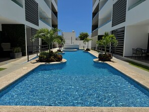 Una piscina con superficie de agua azul cristalina, rodeada de edificios modernos con balcones.
