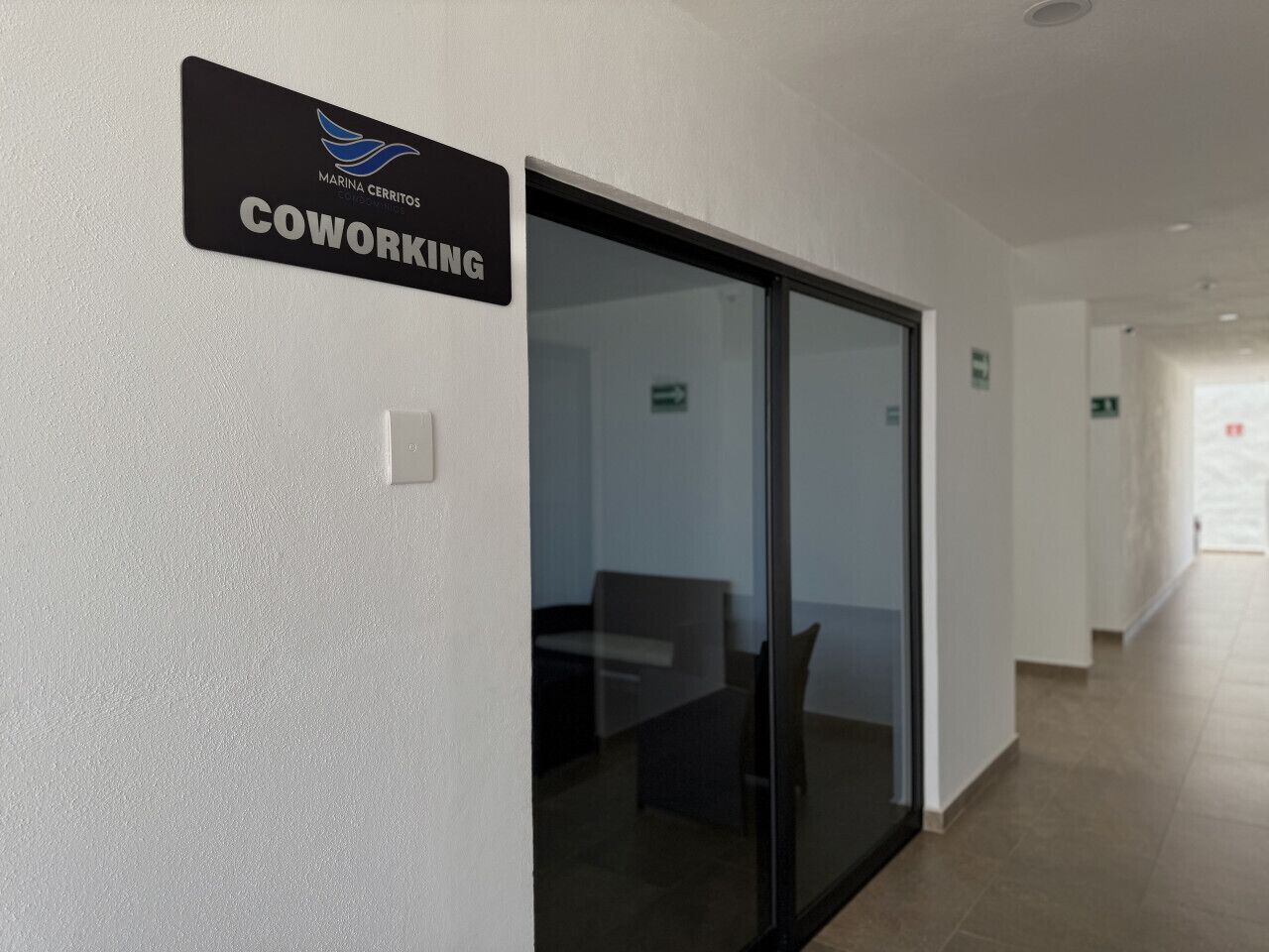 A corridor with a sign indicating a coworking space, a glass door, and a seating area with chairs and a table.