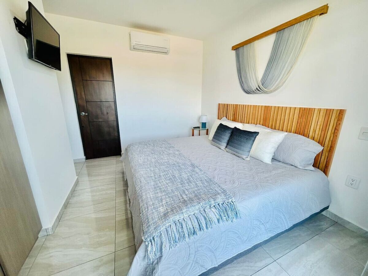 A bedroom with a bed, a TV mounted on the wall, an air conditioning unit, and a wooden headboard.